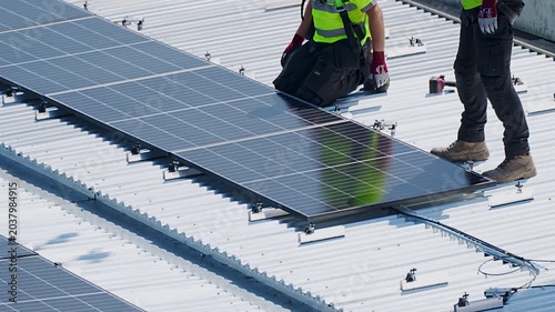 Two worker installing and securing solar panel on rooftop in bright daylight