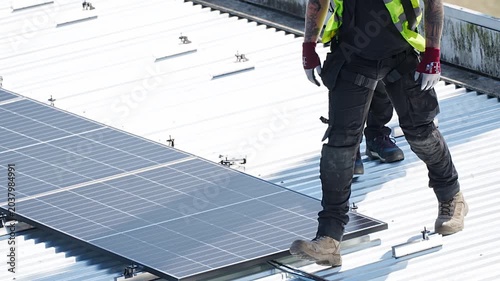 Worker walking on corrugated metal rooftop beside installed solar panel array