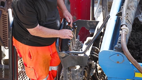 Worker in orange trouser maintaining engine part of heavy machinery at site