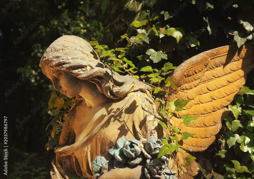 Obraz premium Beautiful guardian angel statue surrounded by ivy and flowers.