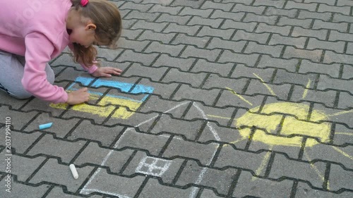 Child Draws With Chalk on Pavement Drawing of House, Sun and Ukrainian Flag. Little Girl Drawing Ukrainian Flag With Chalk. Crisis, Peace, Stop Aggression, Children Against War. Freedom to Ukraine.