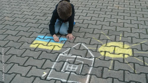 Child Draws With Chalk on Pavement Drawing of House, Sun and Ukrainian Flag. Little Boy Drawing Ukrainian Flag With Chalk. Crisis, Peace, Stop Aggression, Children Against War. Freedom to Ukraine.