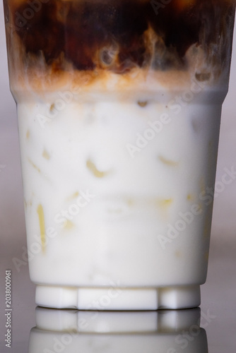 Close-up iced latte coffee showing beautiful layers of dark espresso swirling into white milk with ice cubes inside a plastic cup.