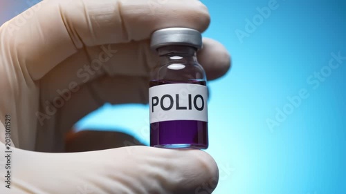 A vial labeled polio contains purple liquid held in a gloved hand.