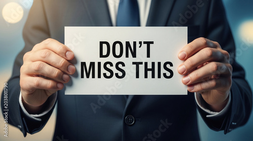 Man in suit holding sign saying DON'T MISS THIS, promoting opportunity or event, professional business context, focus on hands and message.