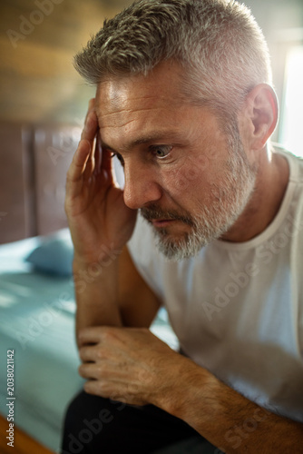 Photos Concerned middle-aged man with headache in bedroom