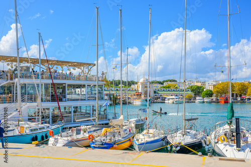 A floating seaside cafe with rooftop garden and patio at the busy Mandraki Harbor with the Nea Agora New Market behind, in Rhodes, Greece.	