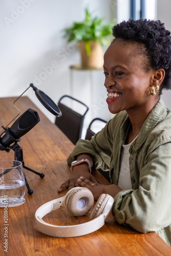 African American female smiling leaning recording podcast in studio in olive jacket with mic