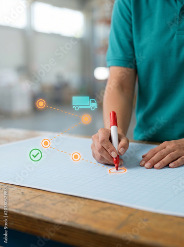 Logistics manager holding marker to plan shipping route on blueprint with glowing delivery truck and location tracking pinpoint icons for supply chain warehouse management