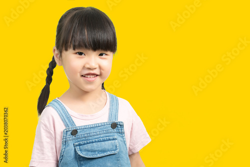 Close-up portrait of a charming young girl with pigtails smiling sweetly against a solid yellow backdrop.