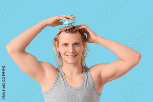 Young blonde man using hair scalp massager on blue background