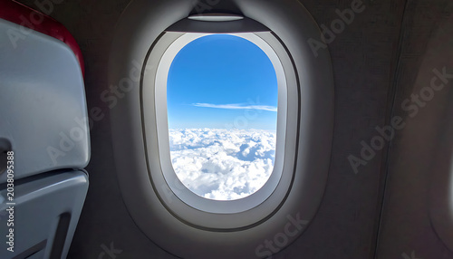 View from airplane window at blue sky and white clouds, seat in foreground, travel and flight concept