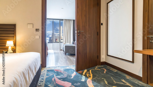 View into a hotel room interior, modern design, open door revealing bed and living area with city view at night