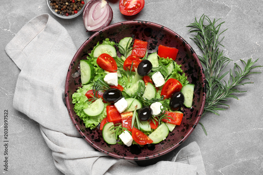 Obraz premium Bowl of tasty Greek salad, rosemary, vegetables and peppercorns on grunge background