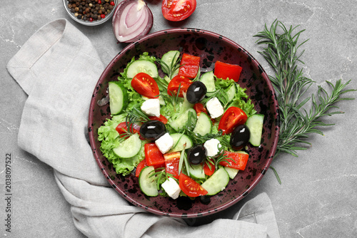 Foto Bowl of tasty Greek salad, rosemary, vegetables and  peppercorns on grunge backg