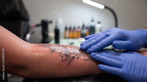 Professional tattoo artist applying healing balm to a new black ink flower tattoo on an arm using nitrile gloves