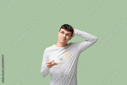 Obraz na płótnie Thoughtful young man with coffee stains on his t-shirt on green background