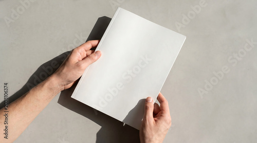 Top View of Hands Holding Blank White Magazine Book Cover Mockup on Concrete Surface with Hard Shadows