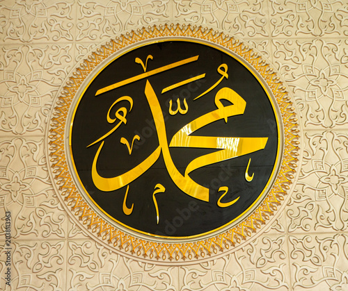 Obraz na płótnie Golden Arabic calligraphy of Prophet Muhammad on a black circular plaque, beautifully framed by a cream wall with elaborate embossed Islamic patterns