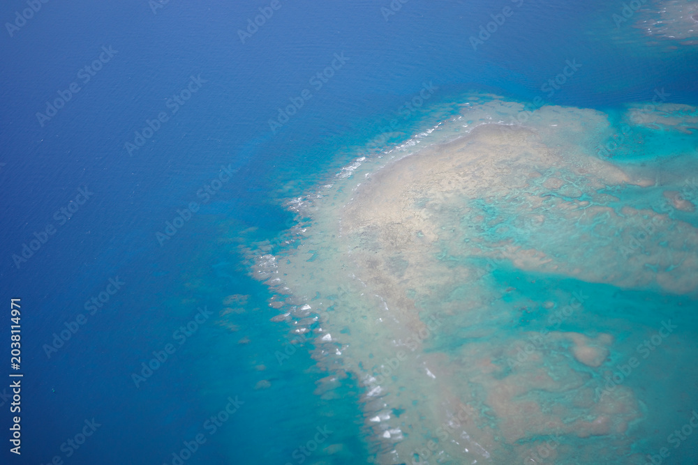 Obraz premium Aerial view of beautiful coral reef and turquoise ocean from airplane window