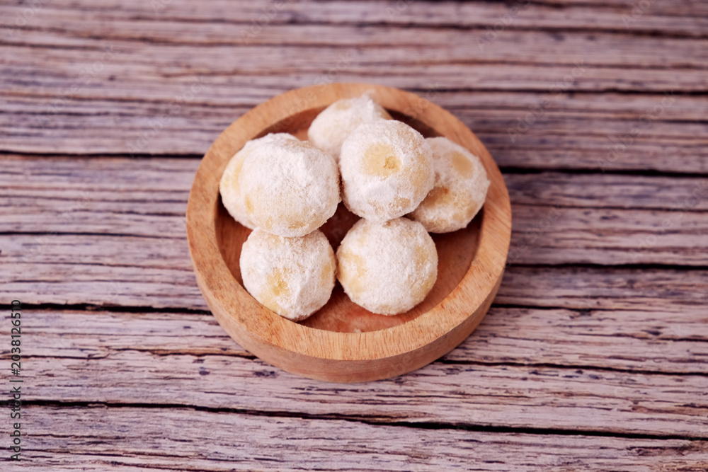 Fototapeta premium Kue Salju Soft, powdered treats rest in a wooden bowl. Warm wood grain adds rustic charm. Minimalist background emphasizes sweet delicacy. Gentle lighting enhances inviting texture. Ideal for food 