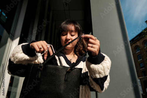 Tableau sur toile Young woman searching everyday handbag for items on street