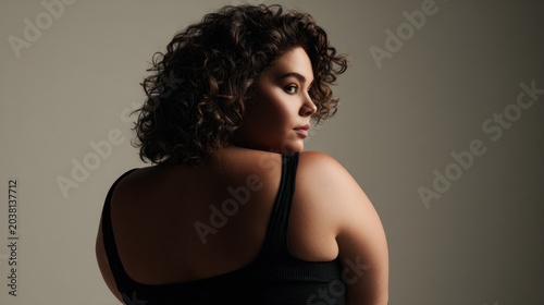 Elegant Woman with Curly Hair Looking Over Shoulder Against Neutral Background
