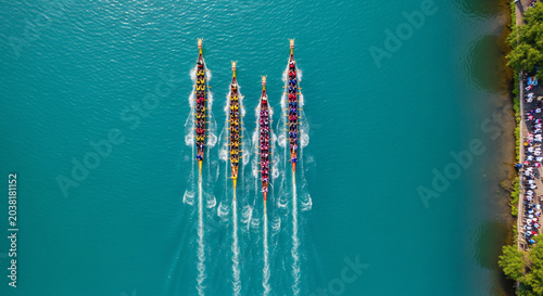 Four vibrant dragon boats race across turquoise water viewed from above.