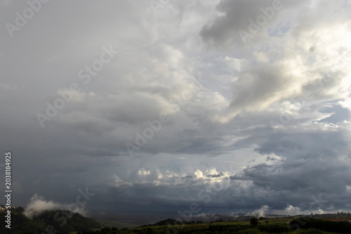 Dramatic dark storm clouds and an approaching rain front move over rolling green hills in a vast rural landscape, showcasing a powerful meteorological event