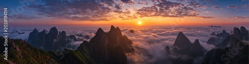 Panoramic sunrise over mountain peaks shrouded in clouds