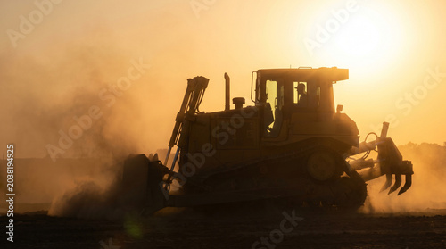 Powerful bulldozer actively reshaping the landscape at golden hour, silhouetted against a radiant sunset while kicking up dust, embodying industrial progress and heavy construction work