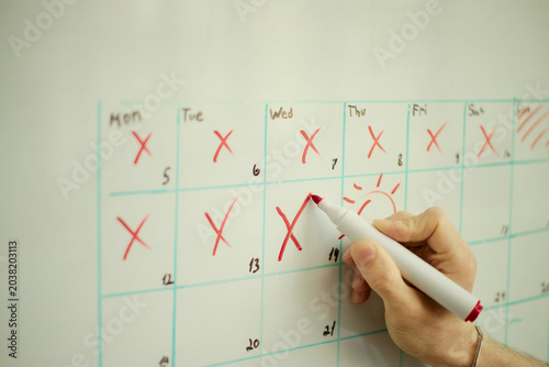 Foto Close up of adult hand marking wall calendar with red pen, crossing off days and planning schedule