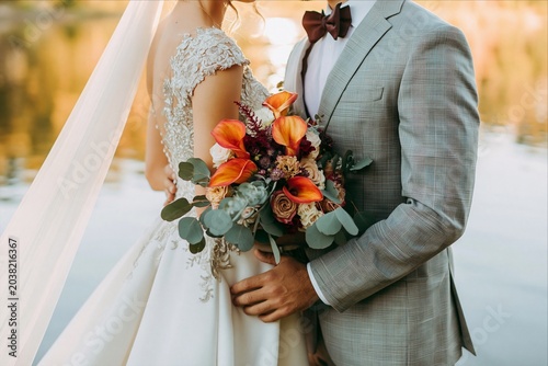 Romantic wedding couple embracing with bridal bouquet at sunset
