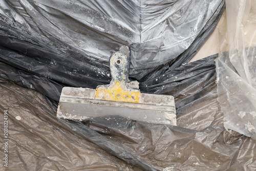 Konstfotografi An old dirty construction spatula with remnants of dry putty and plaster lies on a protective plastic film