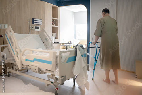Elderly patients in hospital post surgery during recovery period walking with walker in private hospital room showing rehabilitation and mobility support