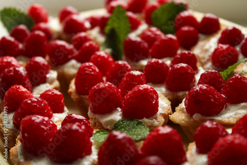 Obraz na płótnie Close-up of fresh raspberry tartlets with creamy filling and mint garnish, featuring shallow depth of field and soft lighting for a gourmet dessert theme