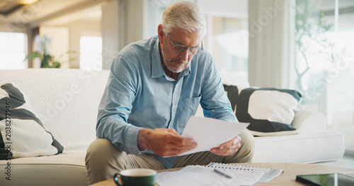 Reading, documents and senior man on sofa with planning for insurance, retirement or assets in home. Policy, pension letter and person with paperwork for financial investment, savings or mortgage