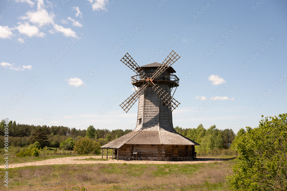 Fototapeta premium Rustic wooden windmill in countryside landscape with clear blue sky
