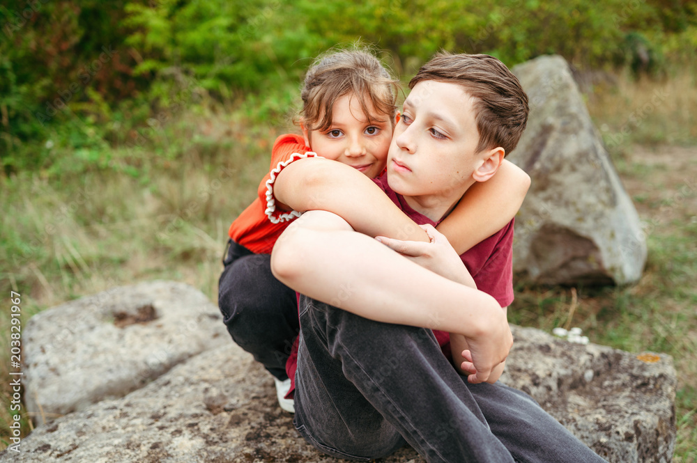 © Cavan - Child girl hugging teenager brother during peaceful countryside moment