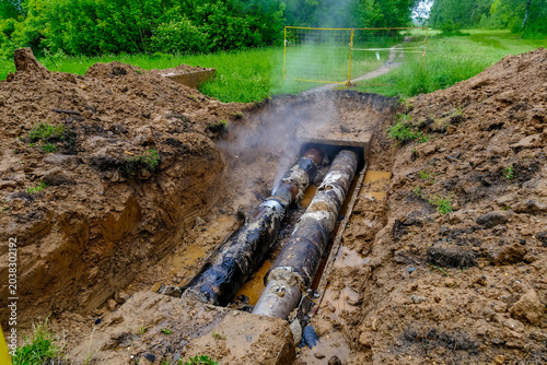Foto Exposed worn heating pipelines in muddy excavation trench after hot water leak and utility failure
