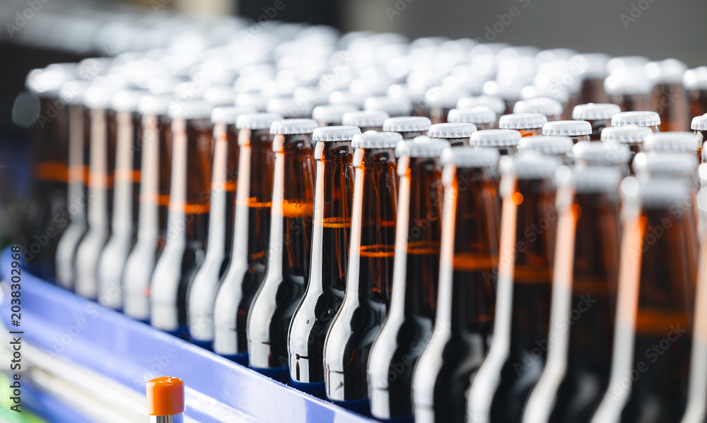 Fototapeta premium Assembly line of brown glass beer bottles in brewery factory