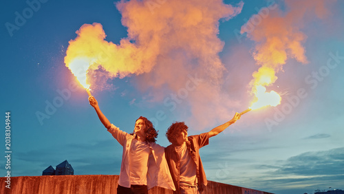 Tableau sur toile Two young men in their late teens or early twenties, stand against a twilight sky, each holding a flaming torch