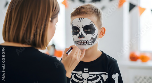 Mother applying halloween skull face paint to her young son for trick or treating