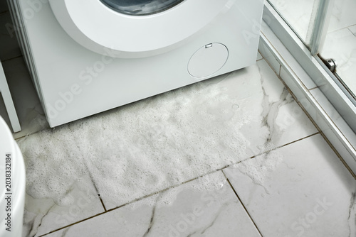 Fotografía Water with detergent flows out from the bottom of the washing machine onto the floor