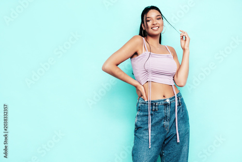Young beautiful smiling female in trendy summer jeans and top clothes. Carefree woman posing near blue wall in studio. Sexy positive model having fun indoors. Cheerful and happy