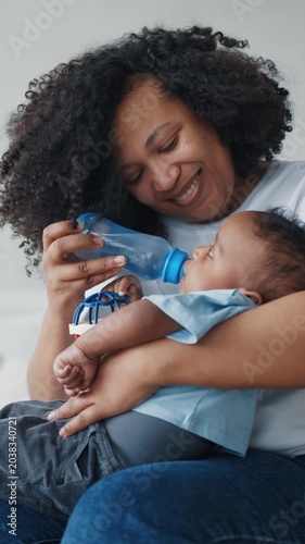 Cute healthy baby drinking water or formula from bottle, mother feeding child. Motherhood and childhood, african american mom practice bottle-feeding, enjoy happy family moments, calm scene at home