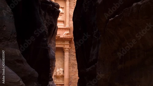 Glimpse of Al-Khazneh Treasury temple through the narrow rocky canyon canyon of the Siq in Petra. Famous ancient archaeological heritage site and wonder of the world in Jordan.