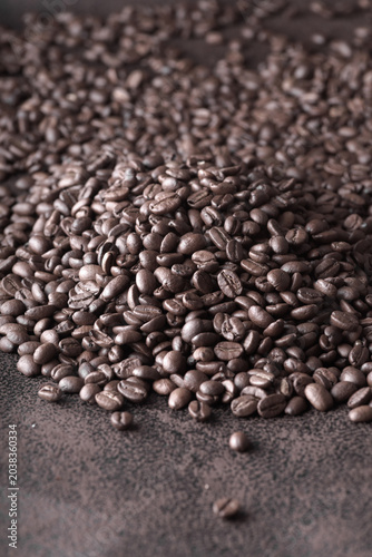 A close-up of dark, freshly roasted coffee beans scattered on a dark background