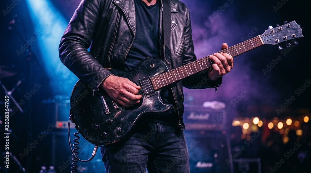 Fototapeta premium Man playing electric guitar on stage with spotlight shining down