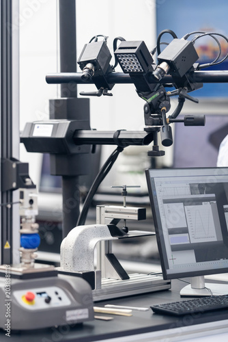 Precision machine vision inspection system with dual camera heads mounted on an adjustable arm, positioned alongside a computer workstation in a controlled laboratory or exhibition environment.